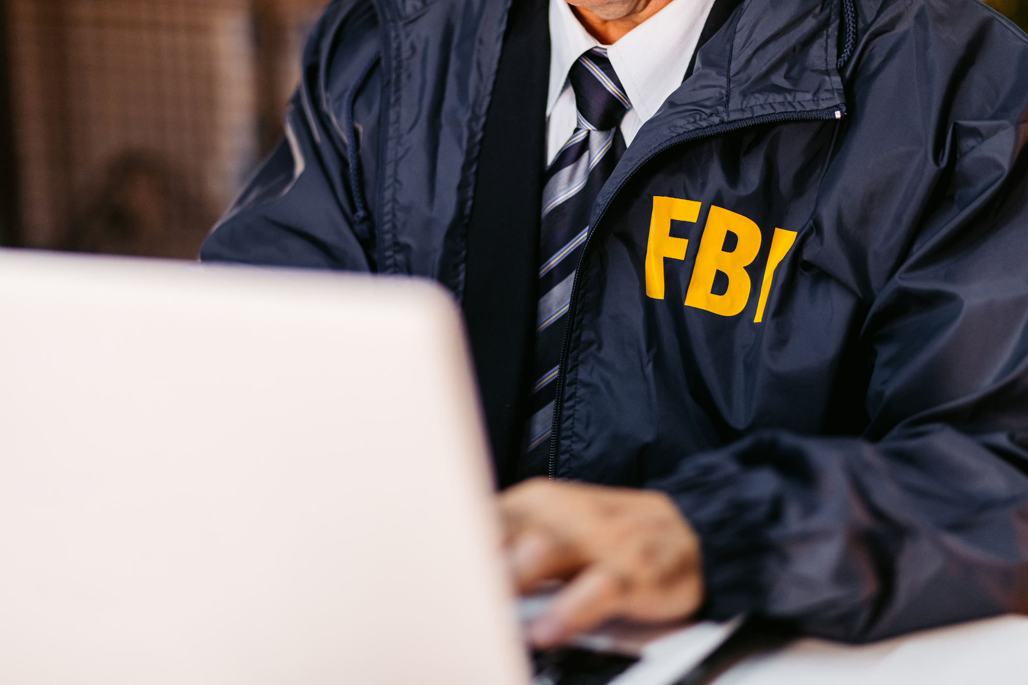 Person in an FBI jacket typing on a laptop. The person's face is not visible