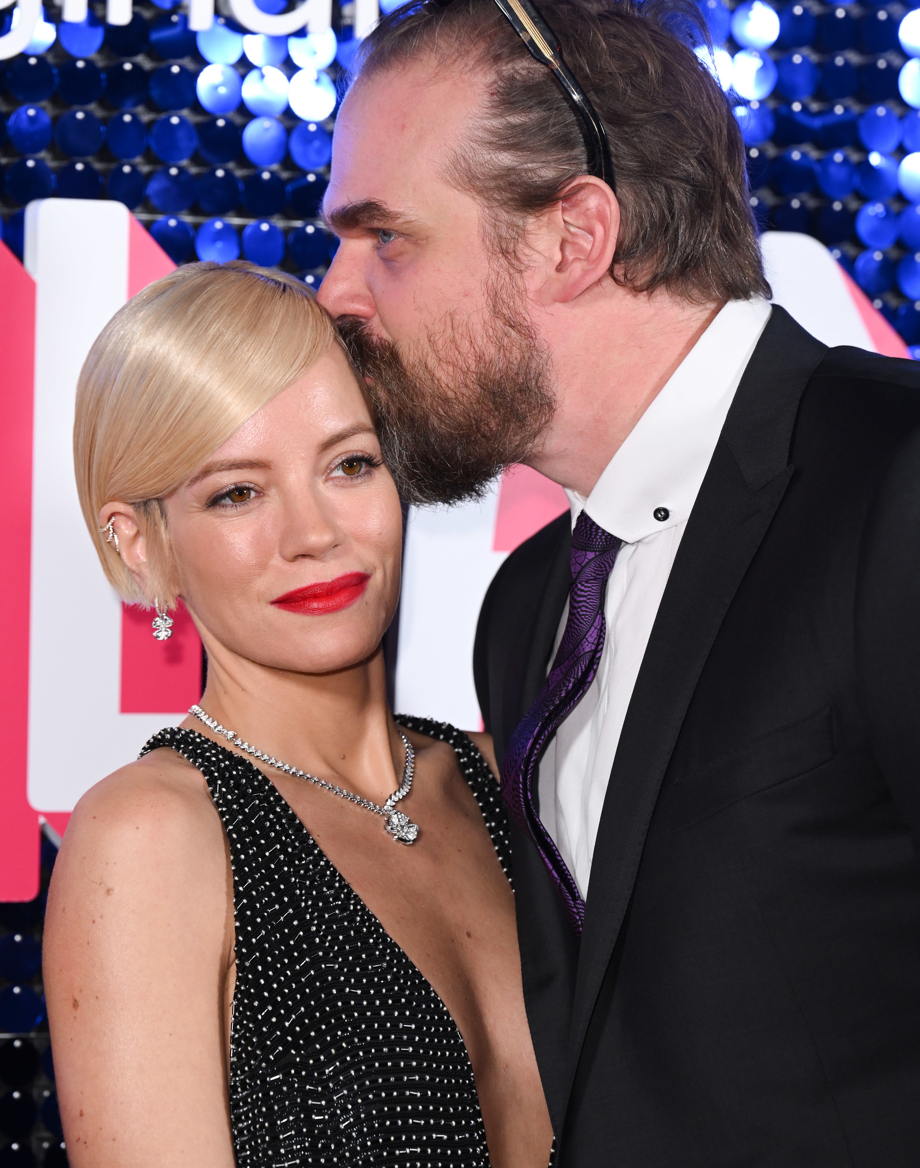 Lily Allen in a sparkling gown and David Harbour in a tuxedo on a red carpet event; David kisses Lily&#x27;s head