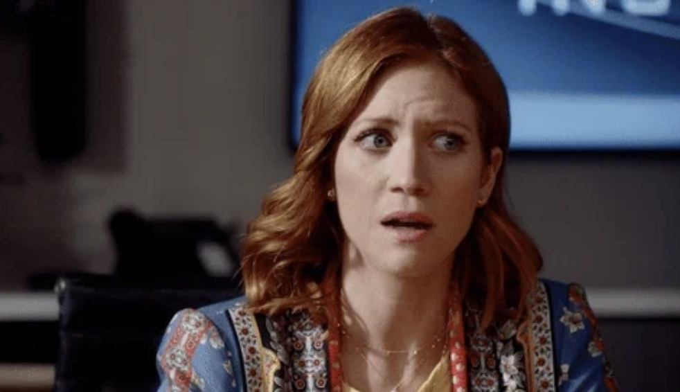 Brittany Snow in a scene from a TV show or movie, wearing a patterned jacket and looking surprised or concerned