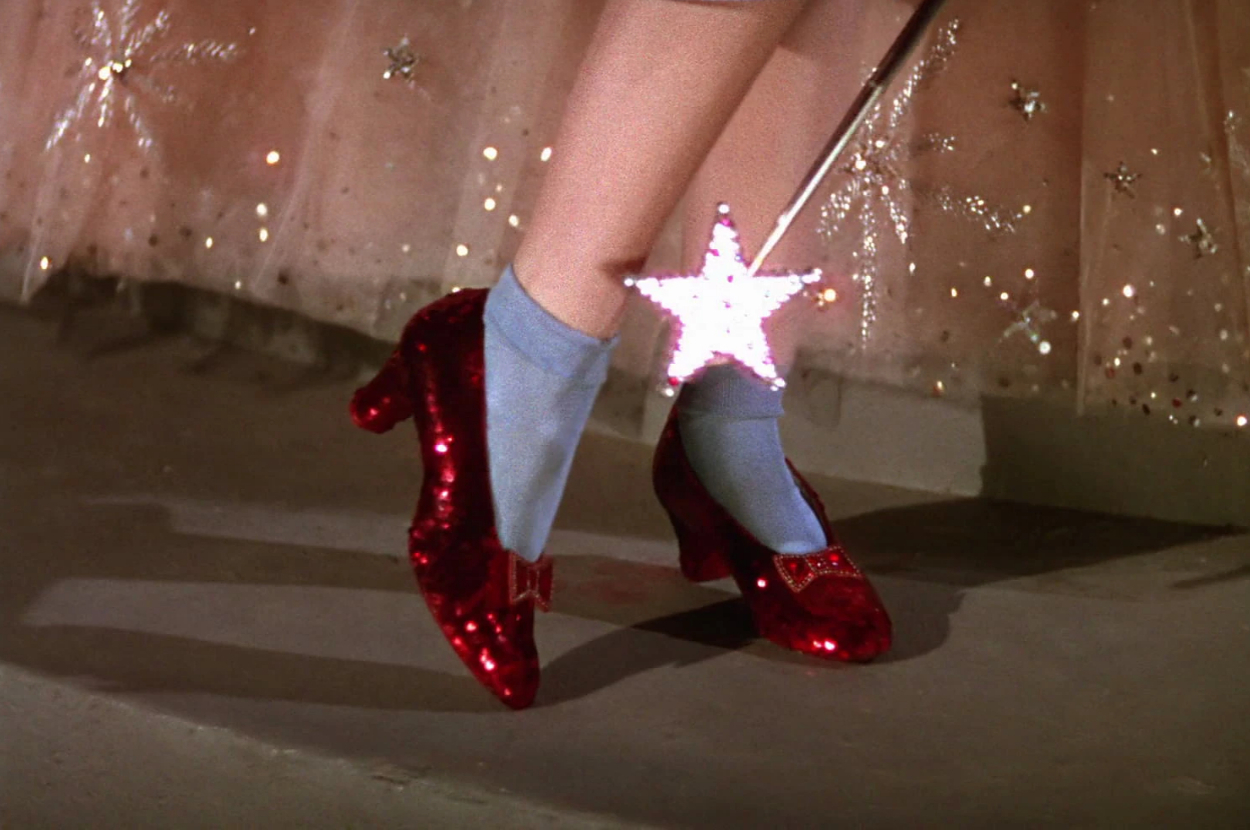 A person wears sparkling red shoes with blue socks. A star-shaped wand hovers over the shoes