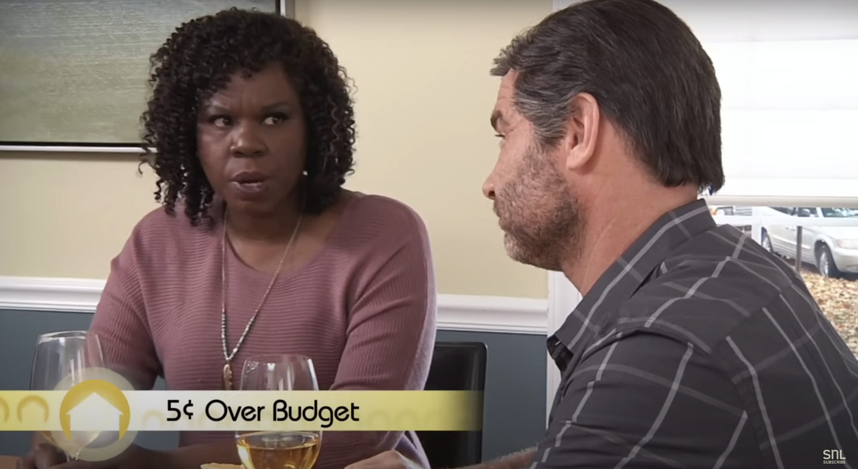 Leslie Jones and Liev Schreiber in a sketch from SNL, sitting at a table with the text &quot;5¢ Over Budget&quot; on screen
