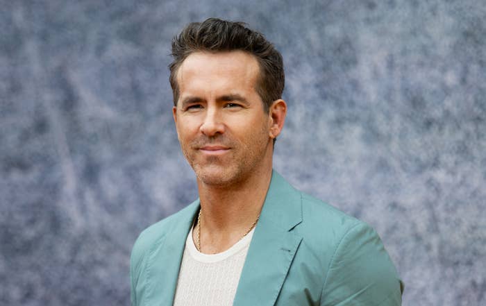 Ryan Reynolds poses in a casual outfit with a textured background