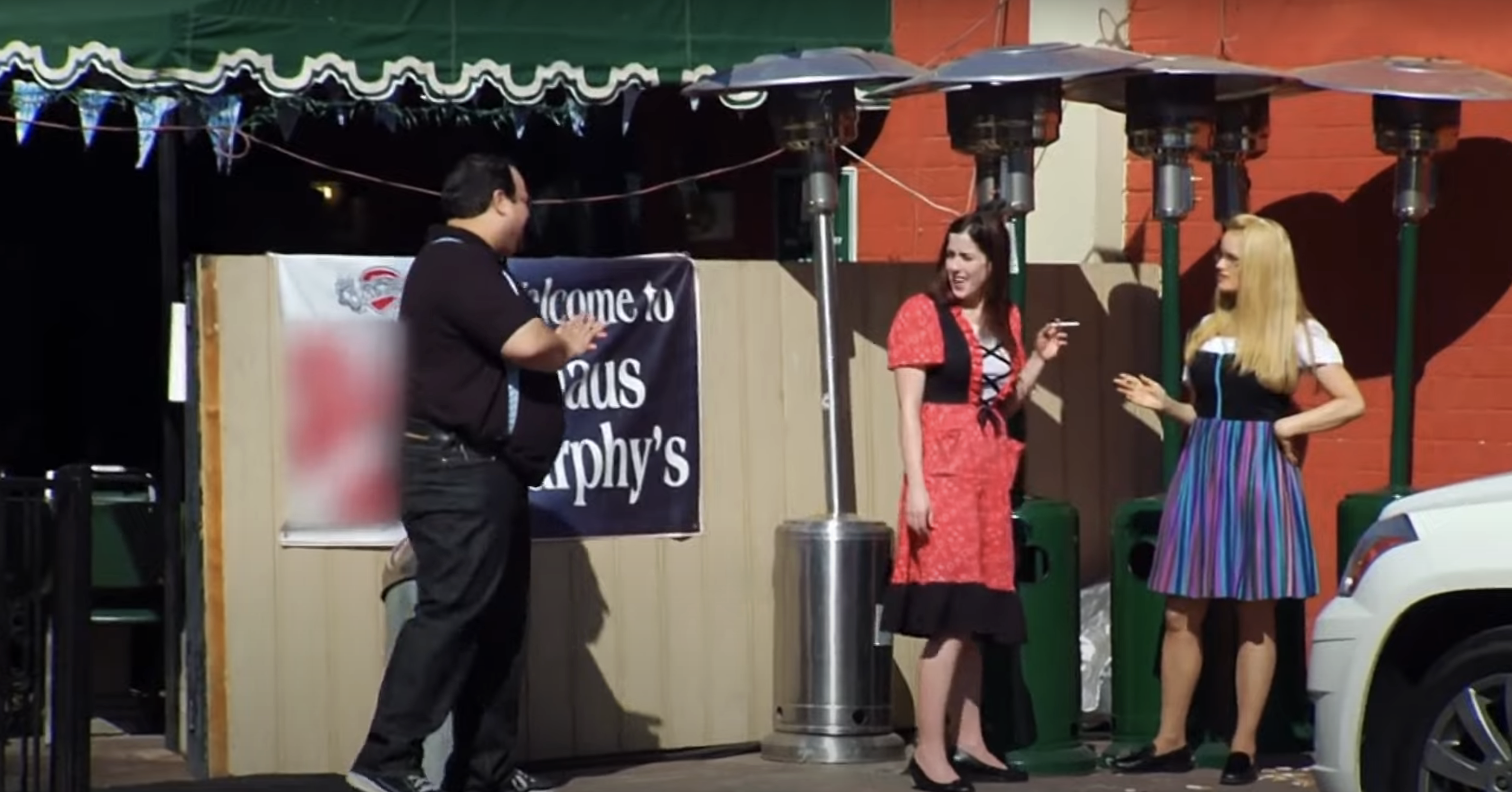 Three people stand outside a restaurant, chatting and smiling; a man on the left, two women on the right in server's uniforms, smoking