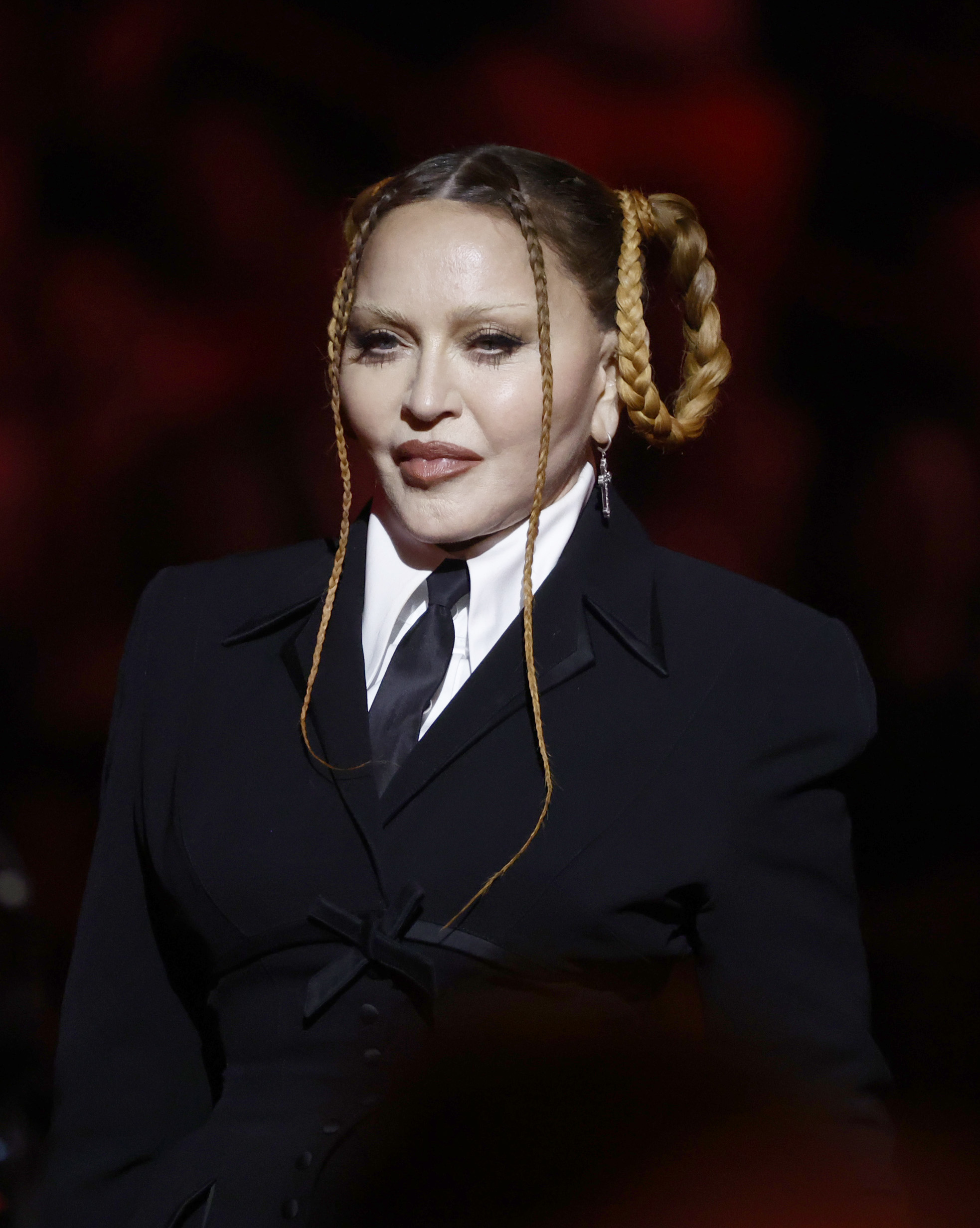 Madonna on the red carpet wearing a suit with a shirt and tie, featuring unique braided hair styled in two buns