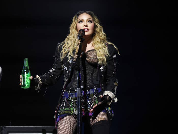 Madonna performs on stage wearing a punk-inspired outfit, holding a bottle and standing in front of a microphone