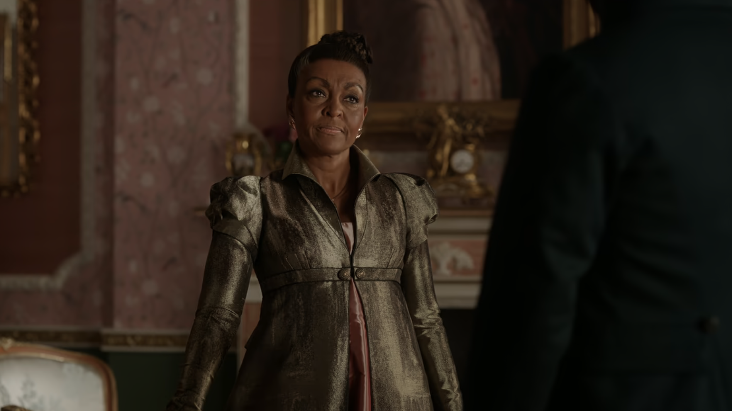 Adjoa Andoh as Lady Danbury stands elegantly in a regal attire, speaking to an unseen character in a scene from the TV series "Bridgerton"