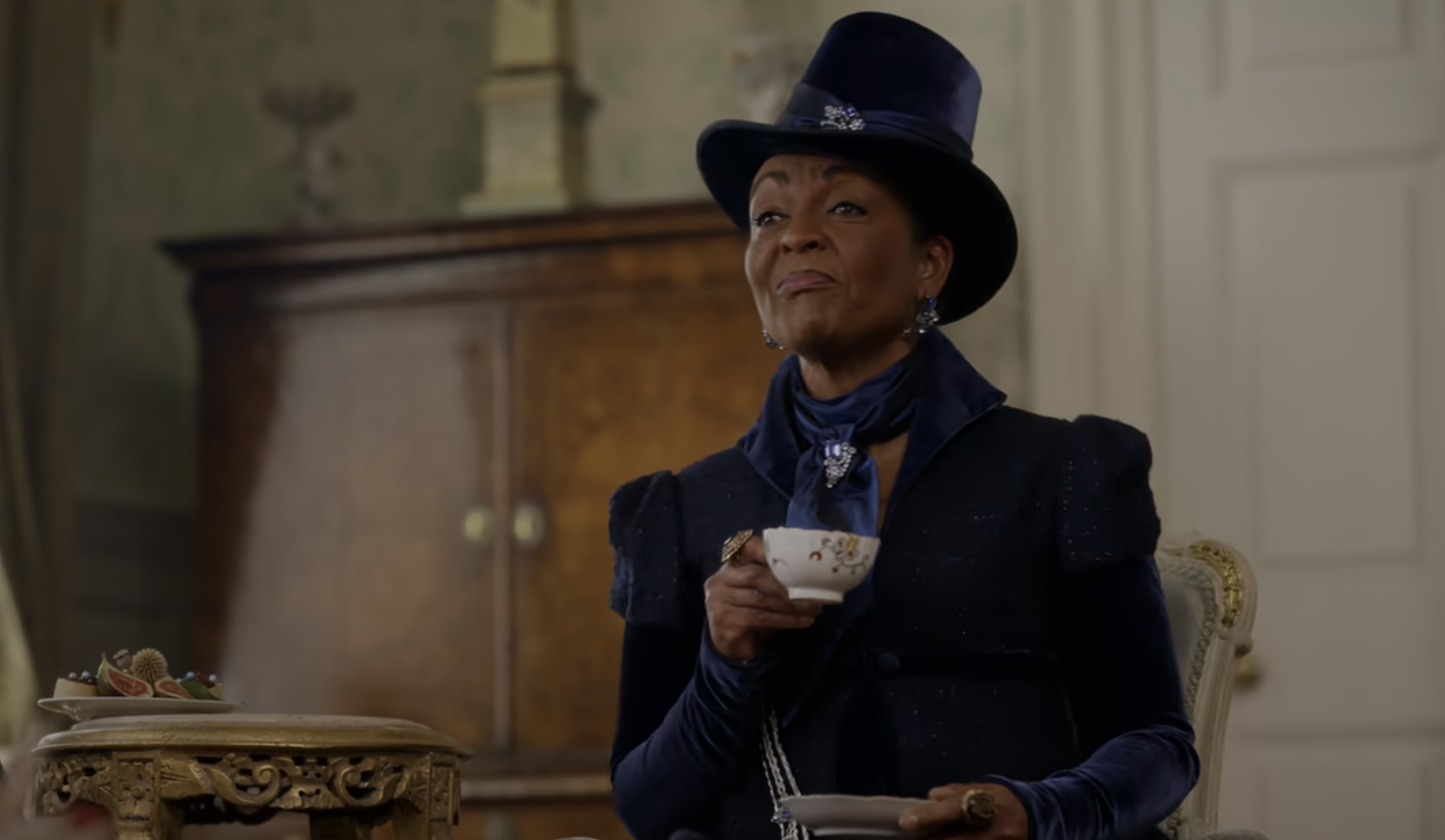 Adjoa Andoh dressed in period clothing, holding a teacup, likely from a scene in a historical drama