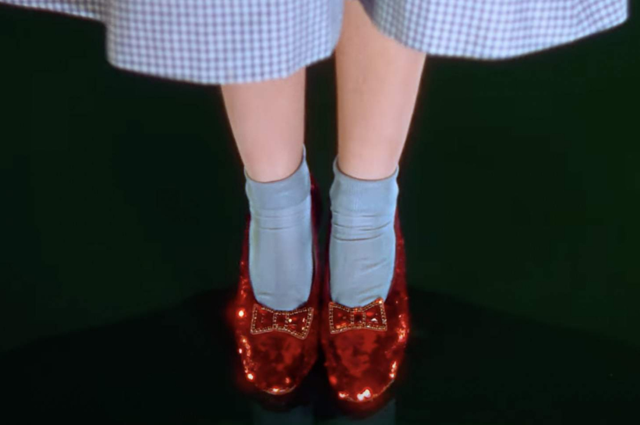 Close-up of Dorothy's legs from The Wizard of Oz, showing her iconic ruby slippers with blue socks and a gingham dress