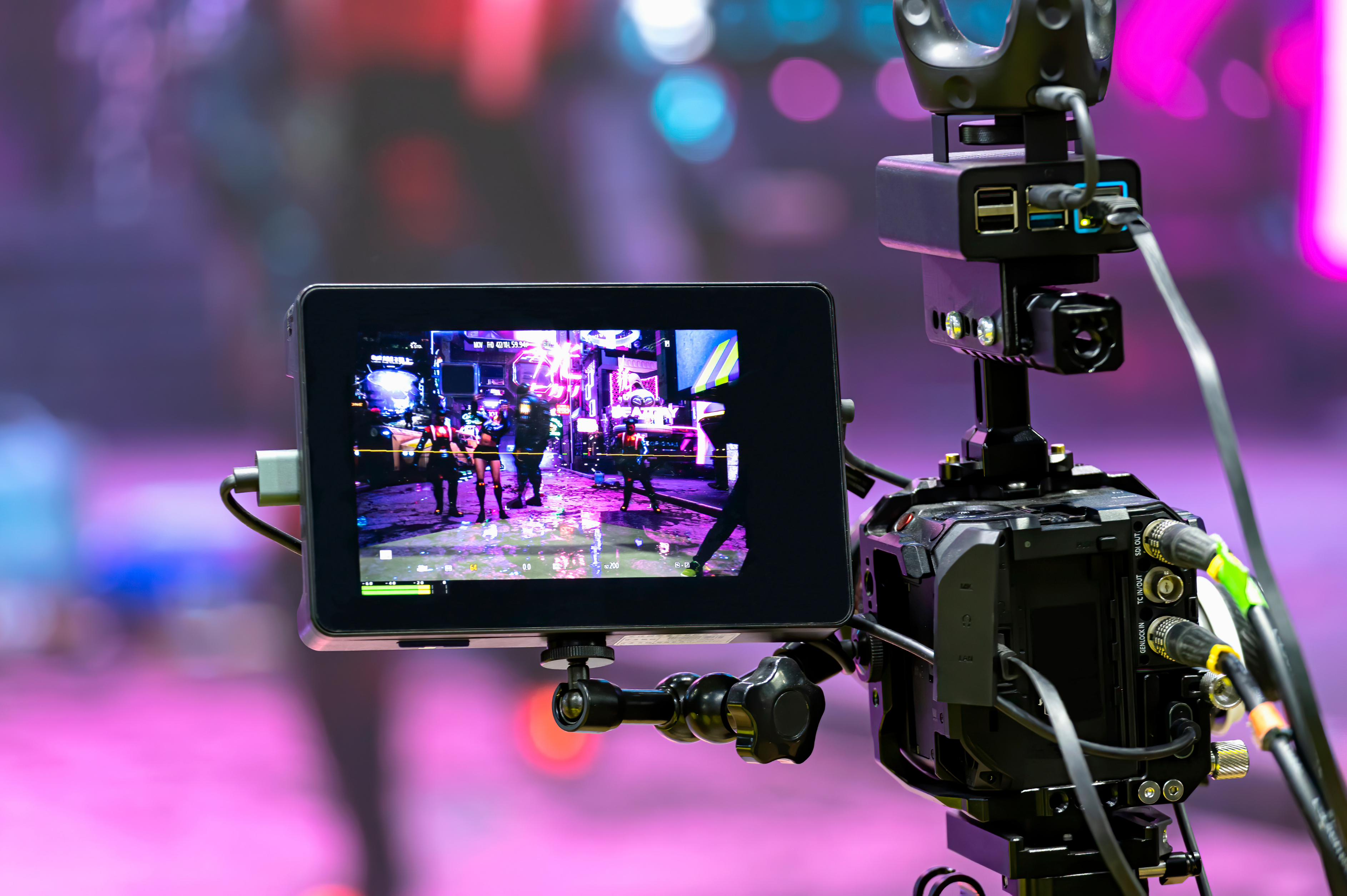 A behind-the-scenes photo shows a camera filming a vibrant, neon-lit street scene with people walking in the background