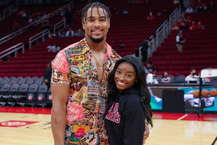 Simone Biles, in a black hoodie, and Jonathan Owens, in a patterned shirt, pose together on a sports court