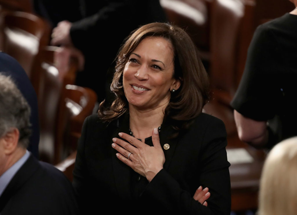 Kamala Harris smiles with her hand on her chest while attending an event, dressed in an elegant black outfit