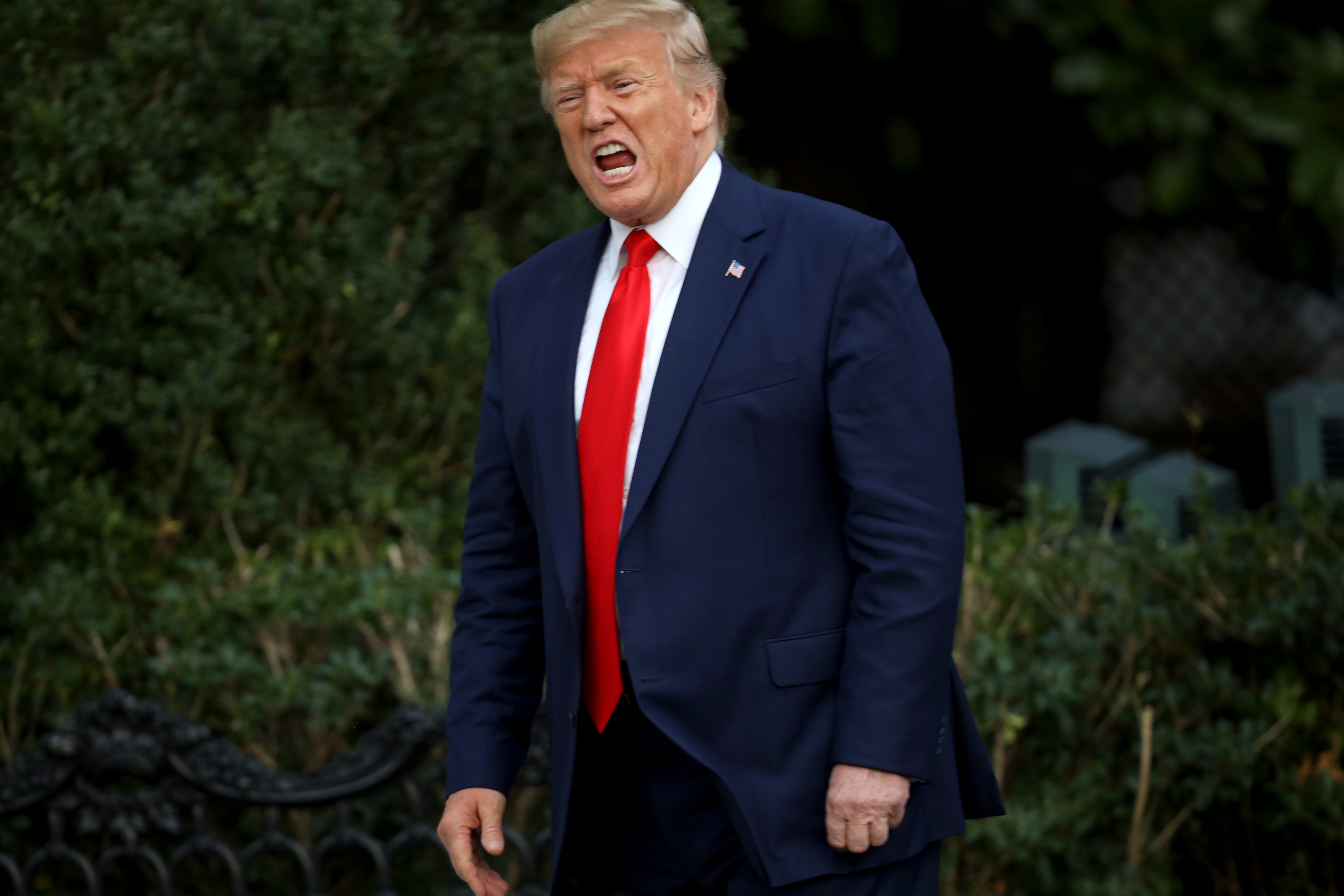 Donald Trump is outdoors, wearing a suit with a red tie, looking animated
