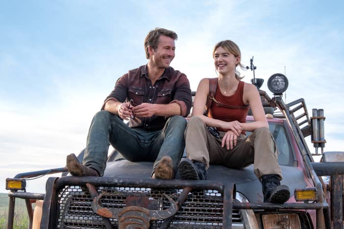 Glen Powell and Daisy Edgar-Jones sit on the hood of a rugged truck, smiling and appearing relaxed, in a scene from Twisters