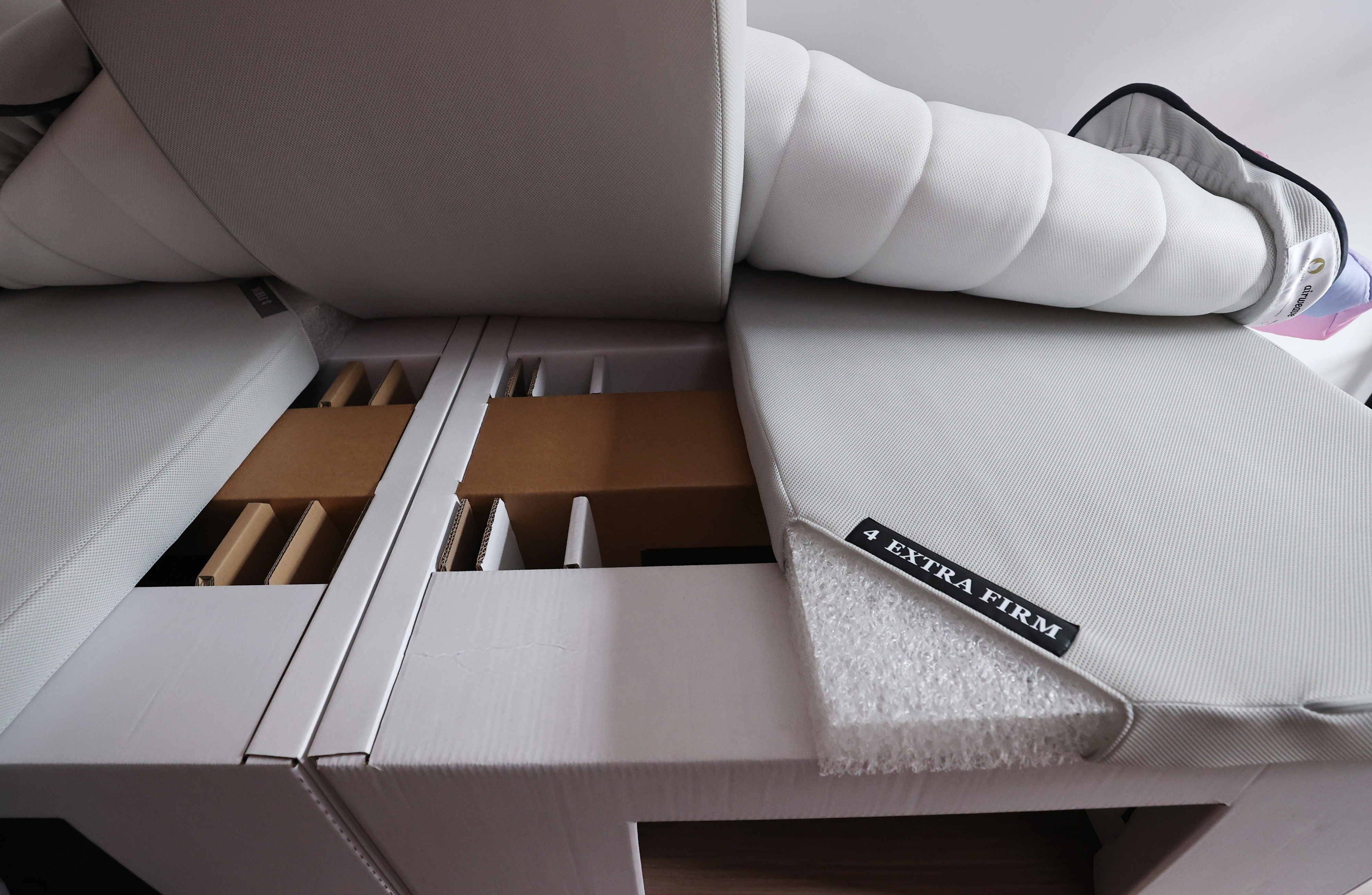 Mattress labeled "Extra Firm" partially removed from its packaging, showing wooden bed frame slats underneath