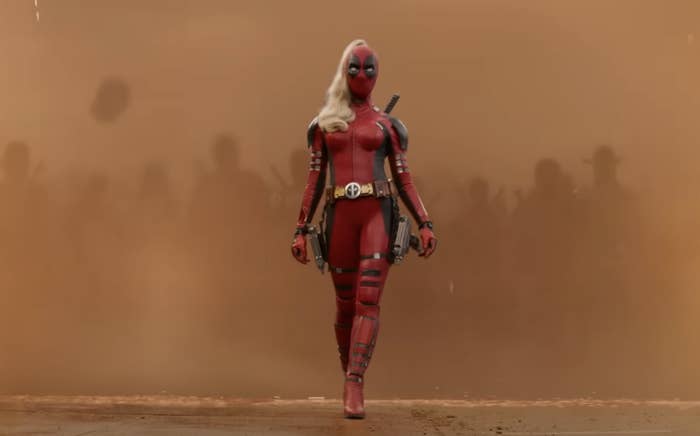 Lady Deadpool, dressed in a red and black suit, confidently walks forward holding weapons, with a smoky background and shadowy figures