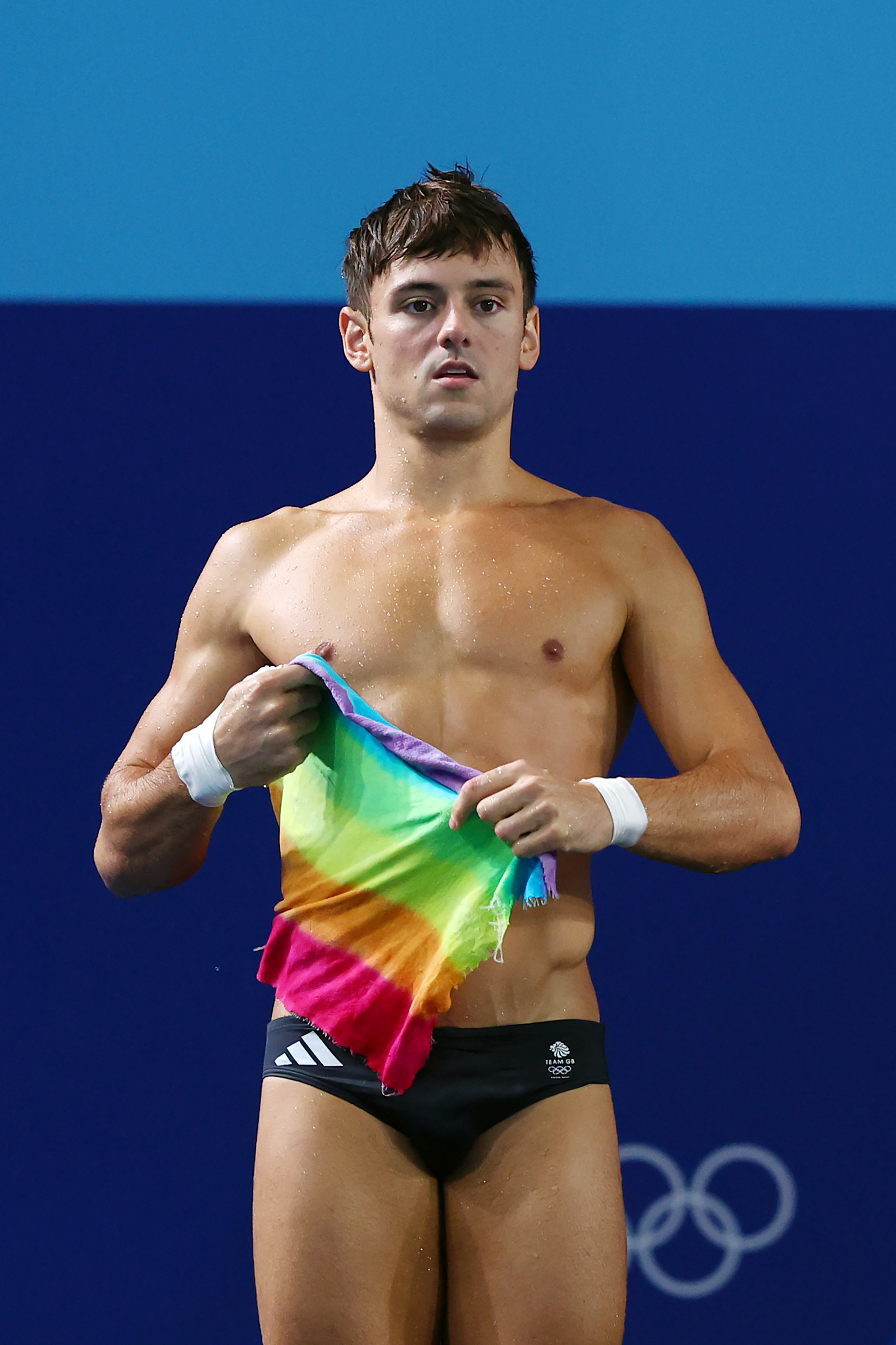 Tom Daley holding a rainbow flag, standing in his swimming trunks at the Olympics