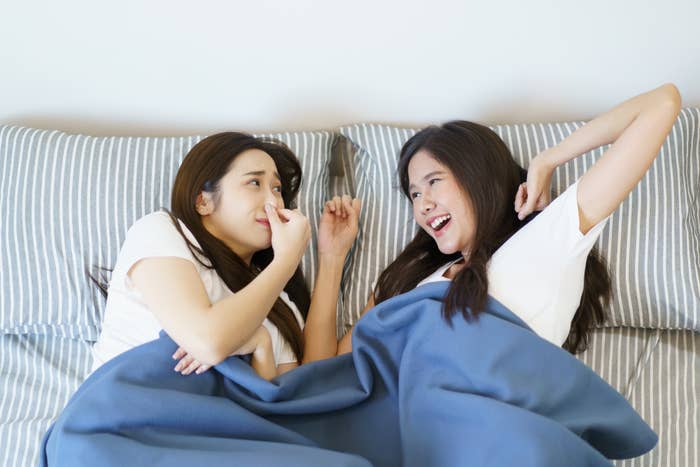 Two women are lying in bed and one of them smells something bad