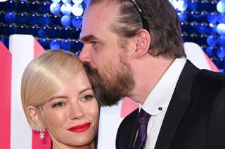 Lily Allen in a sparkling gown and David Harbour in a tuxedo on a red carpet event; David kisses Lily's head