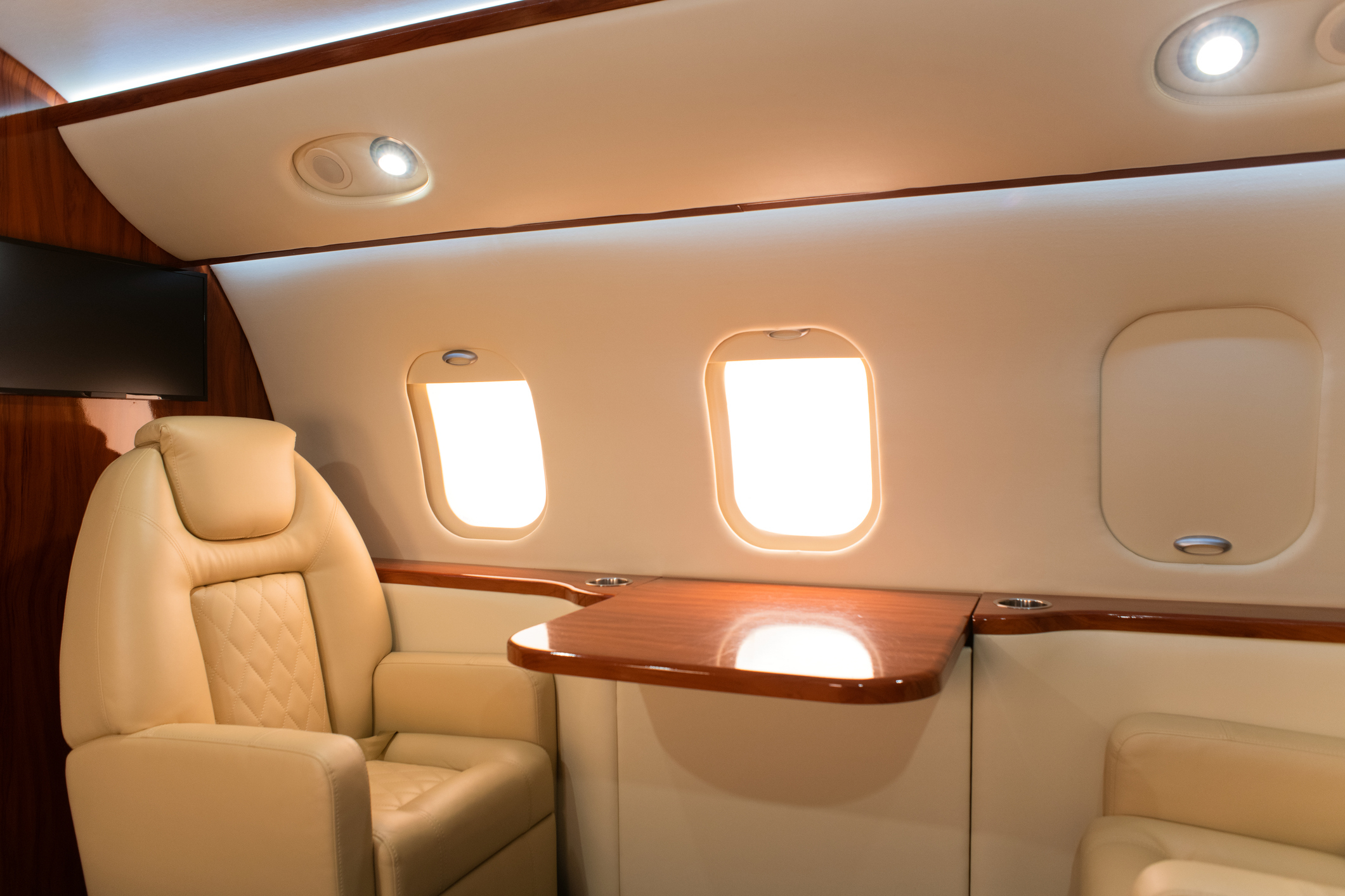 Interior of a private jet showing luxurious leather seats and a wooden table under three windows