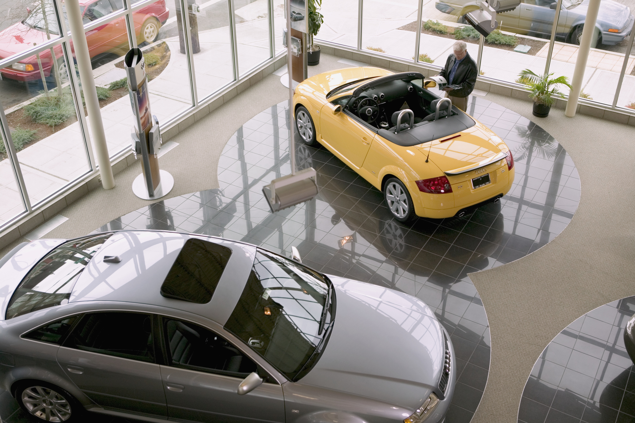 Car showroom with a yellow convertible and a silver sedan. A man is standing near the yellow convertible