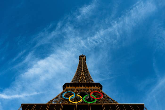 Eiffel Tower base with Olympic rings displayed, viewed from below against a blue sky
