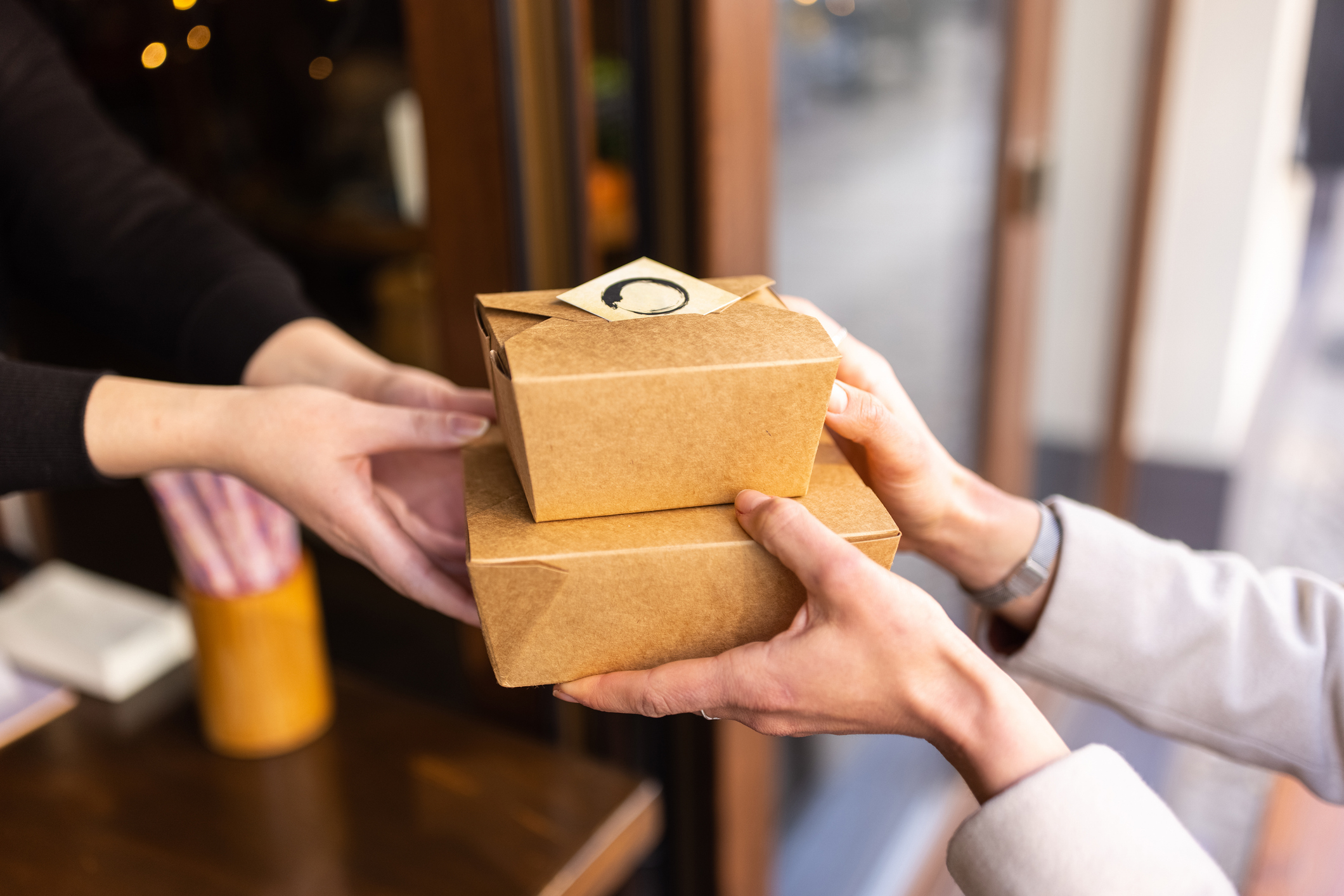 Two people exchanging cardboard food takeout boxes outside a restaurant
