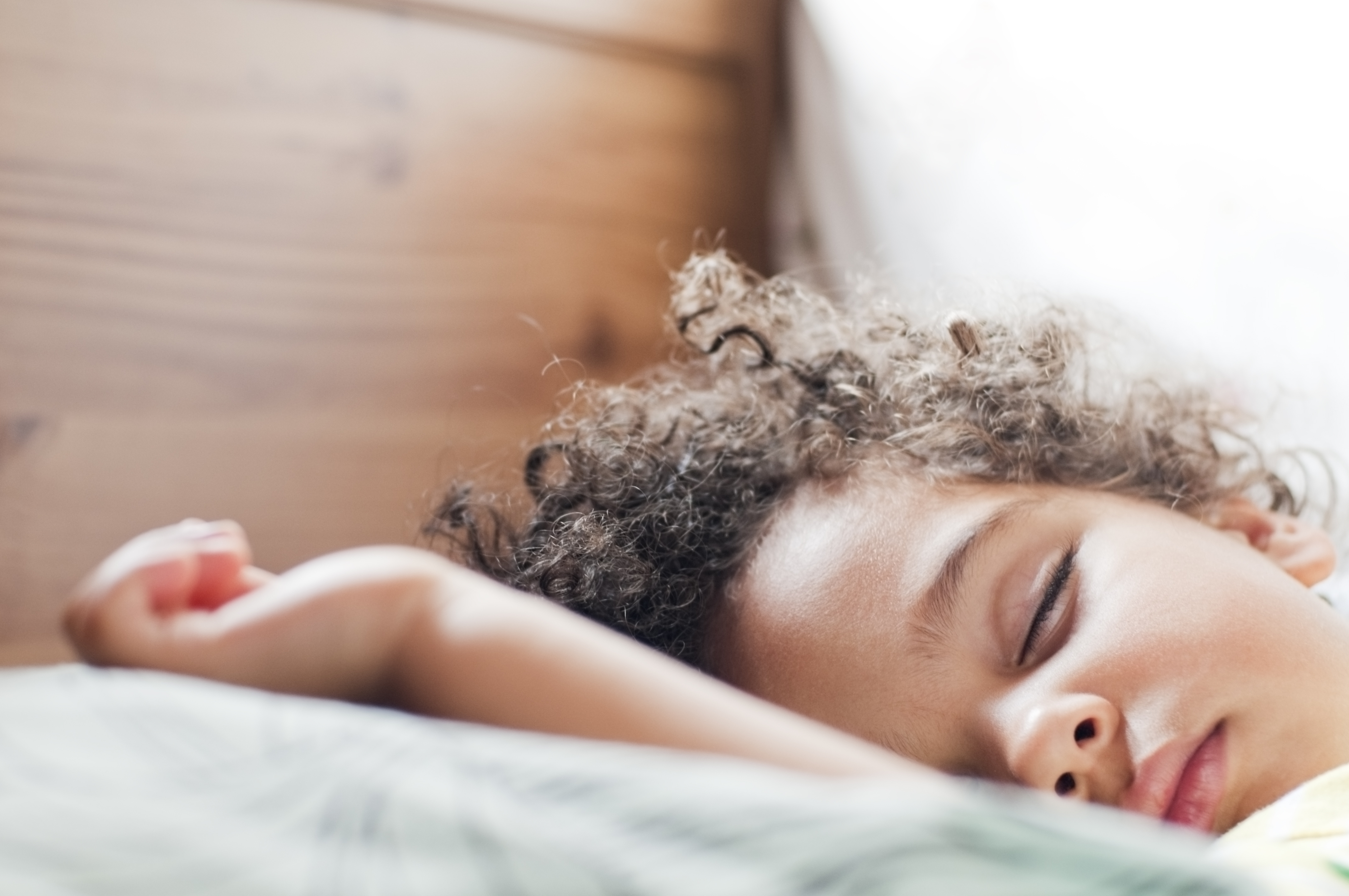 A young child sleeps peacefully on a pillow, lying on their side with curly hair cascading around their face