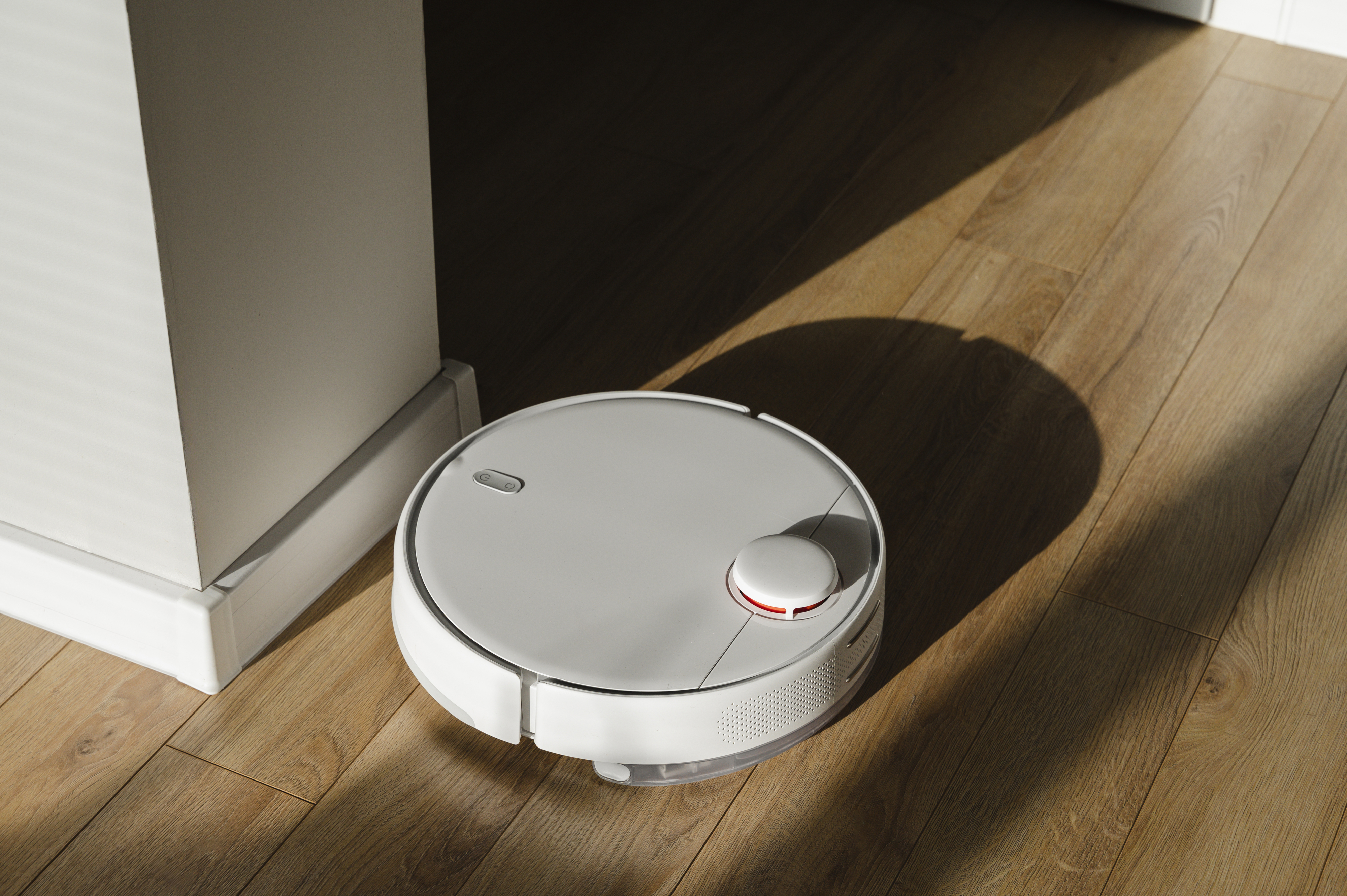 A robotic vacuum cleaner is working on a wooden floor, moving away from a wall