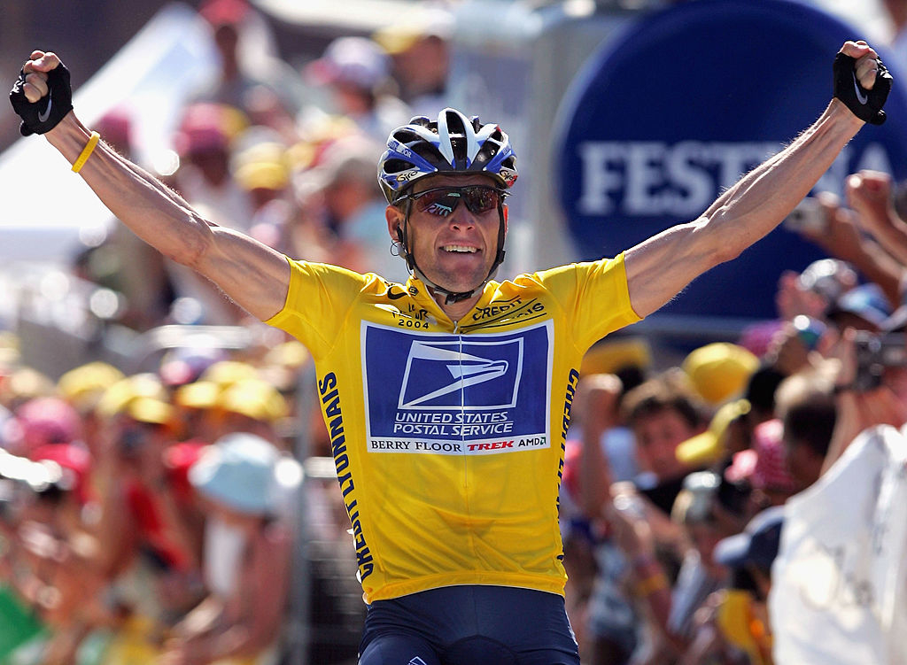Lance Armstrong wearing a yellow United States Postal Service jersey and blue helmet triumphantly raises his arms after a race win