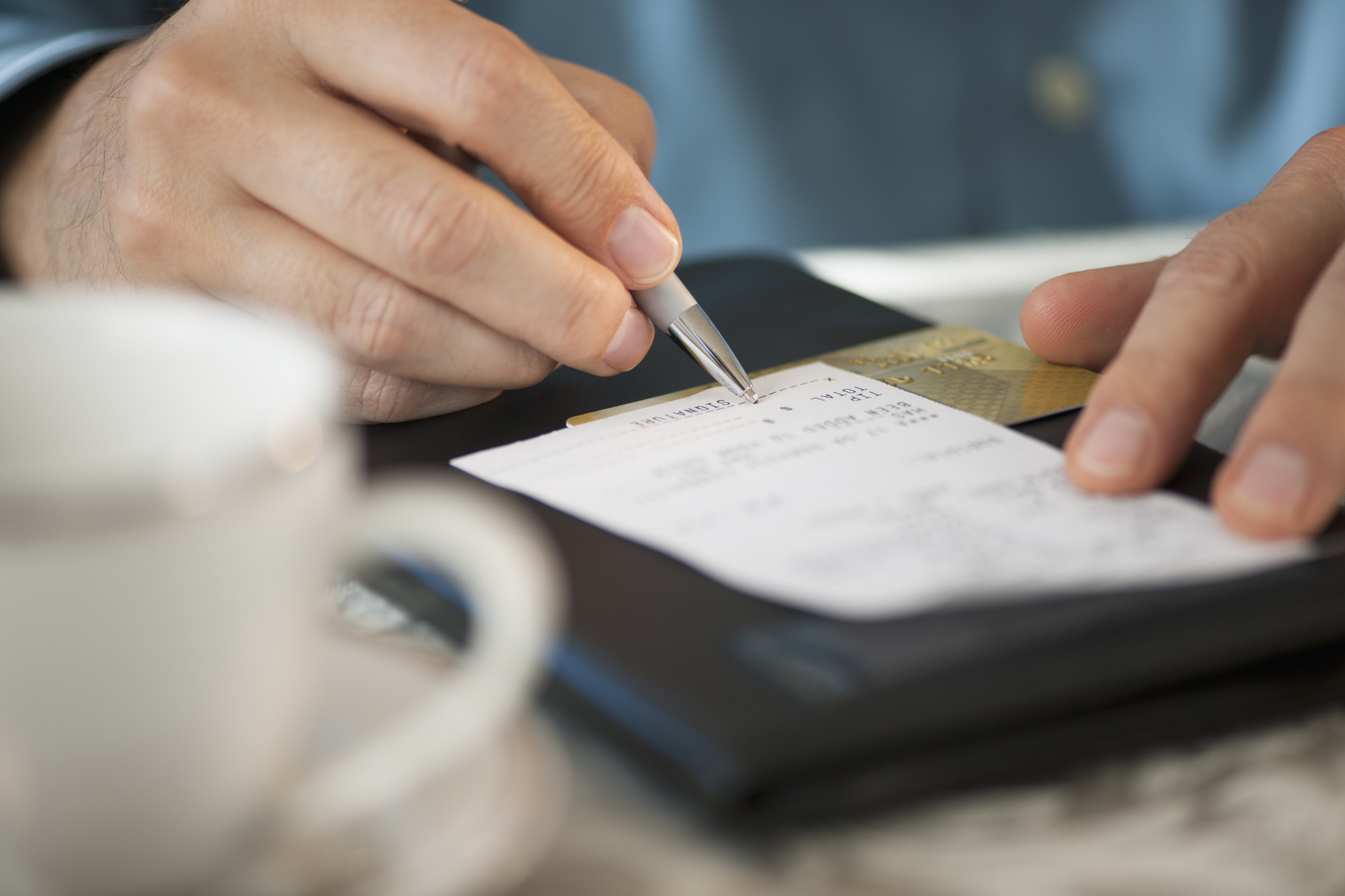 Person signing a receipt at a restaurant table with a credit card and coffee cup placed nearby