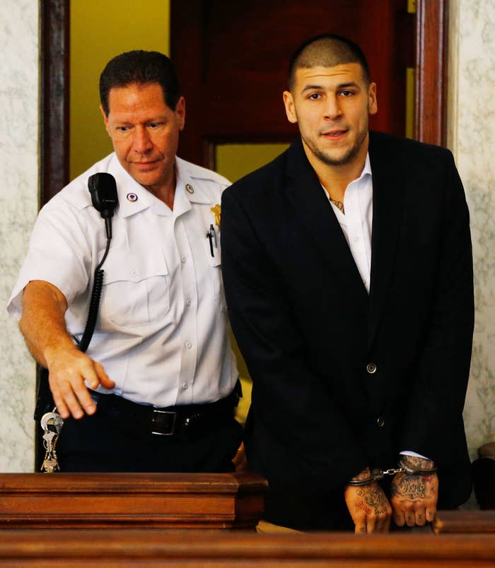 Aaron Hernandez in handcuffs being escorted by a police officer in a courtroom