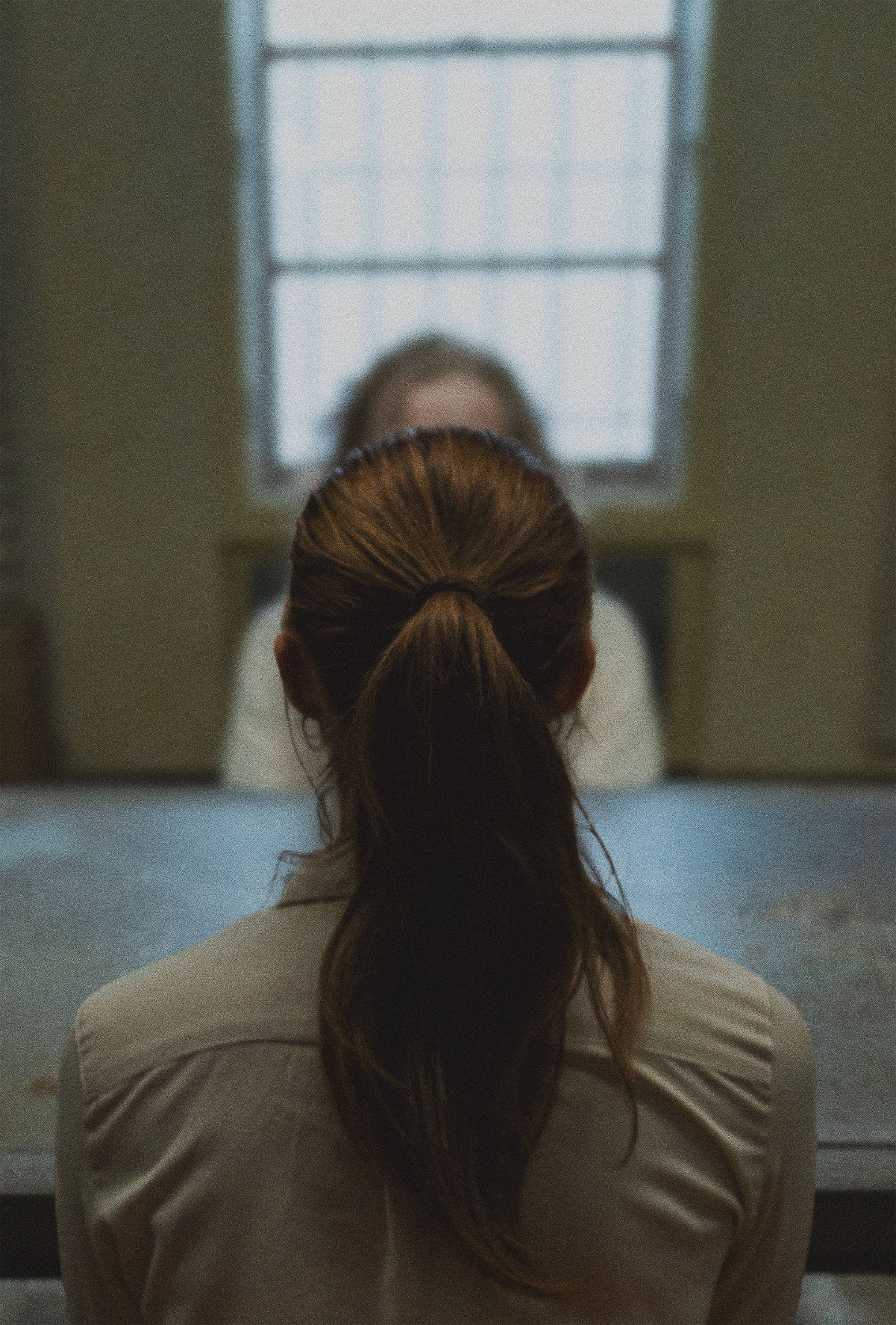 A woman with a ponytail sits across the table from another person in a dimly lit room. Faces are not visible