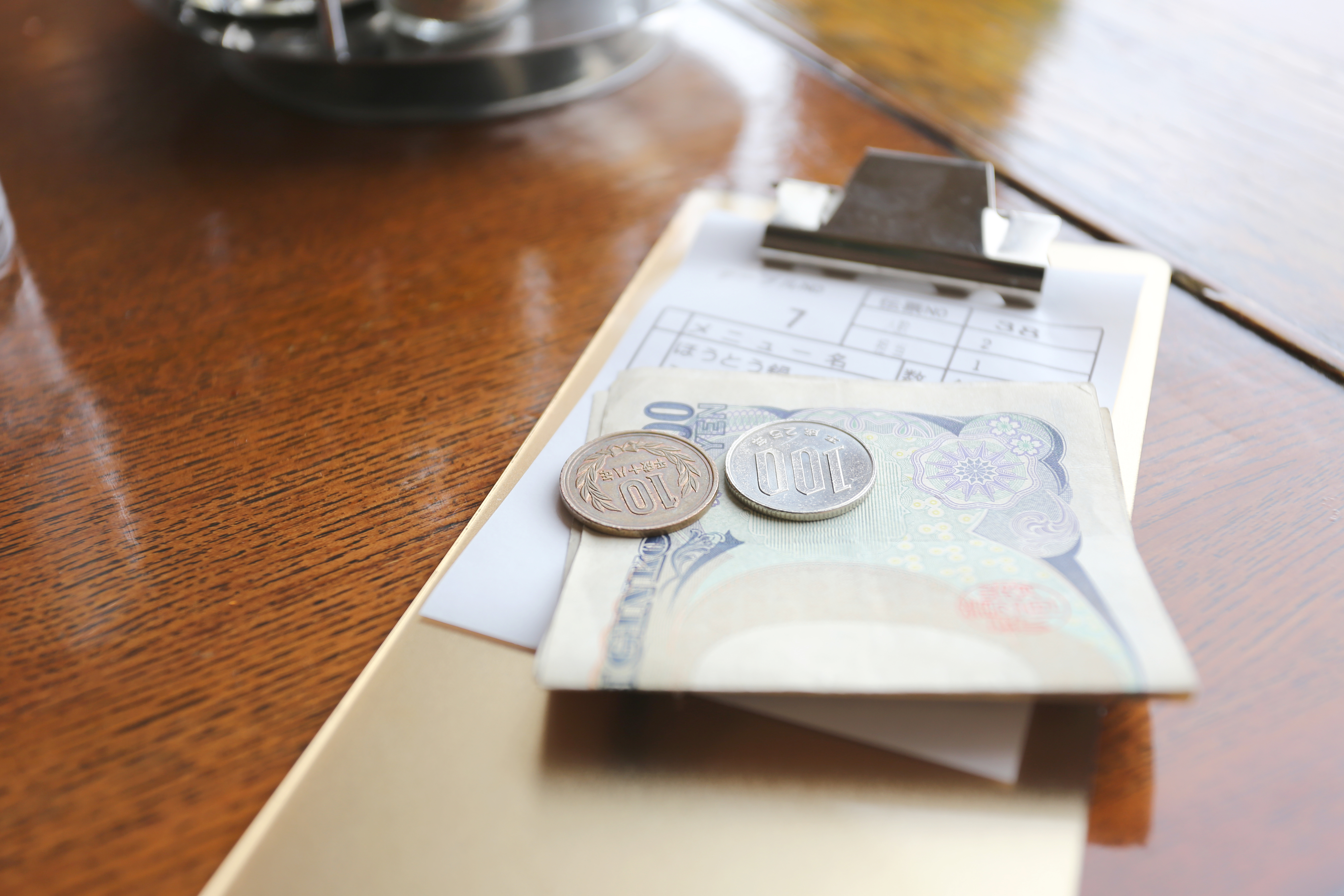 Close-up of a clipboard with a receipt, currency notes, and coins on a wooden table