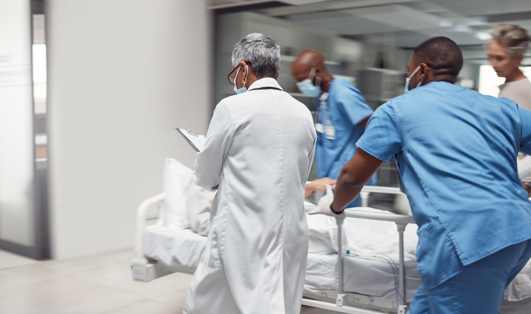Medical team, including a nurse and doctors, rushes a patient on a gurney through a hospital corridor