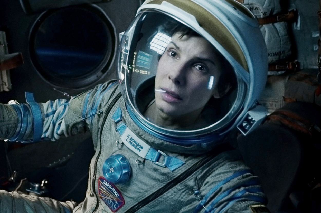 Sandra Bullock, dressed as an astronaut in a space suit, inside a space shuttle cockpit