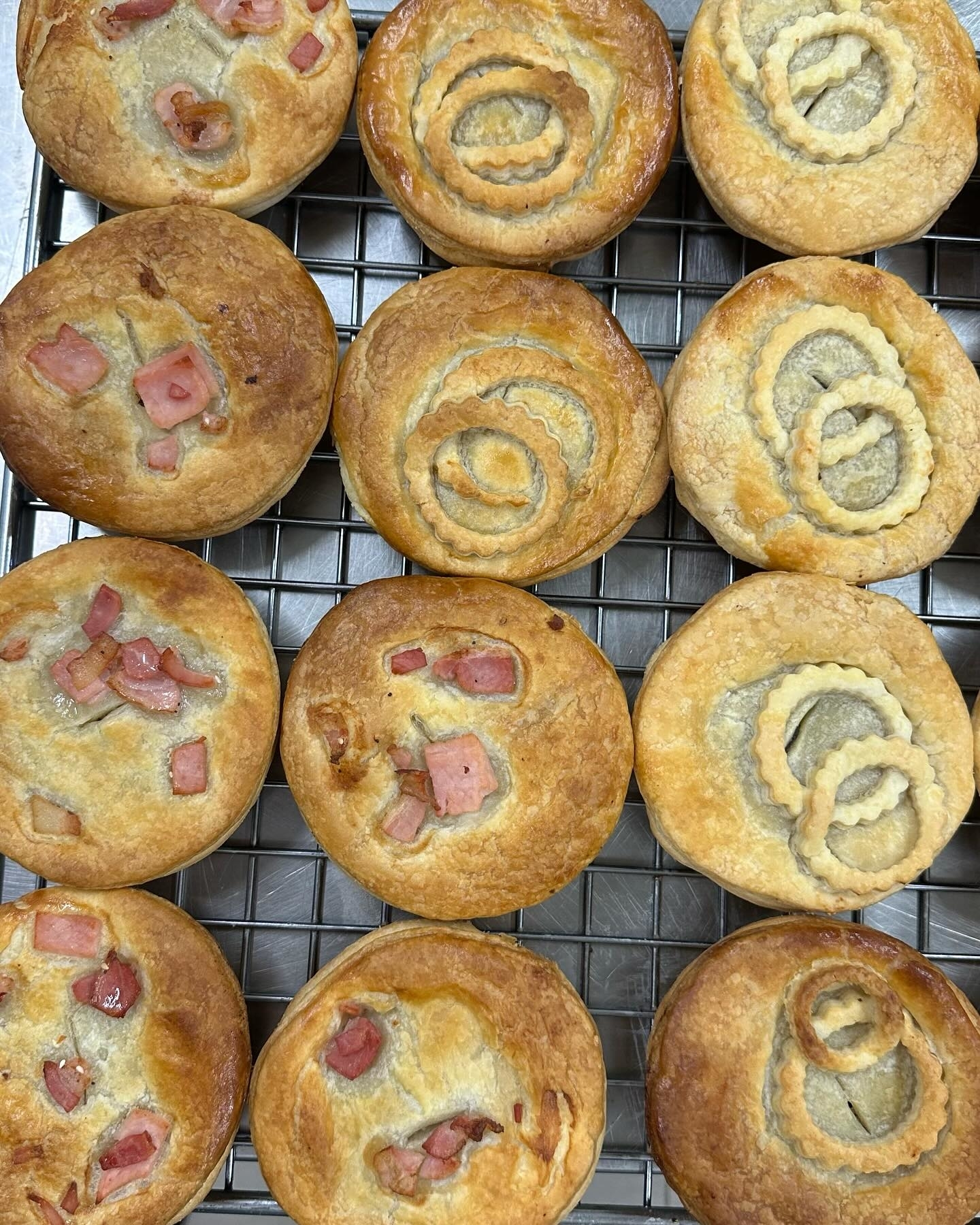 An assortment of savory pastries with different toppings, such as ham and onions, displayed on a cooling rack