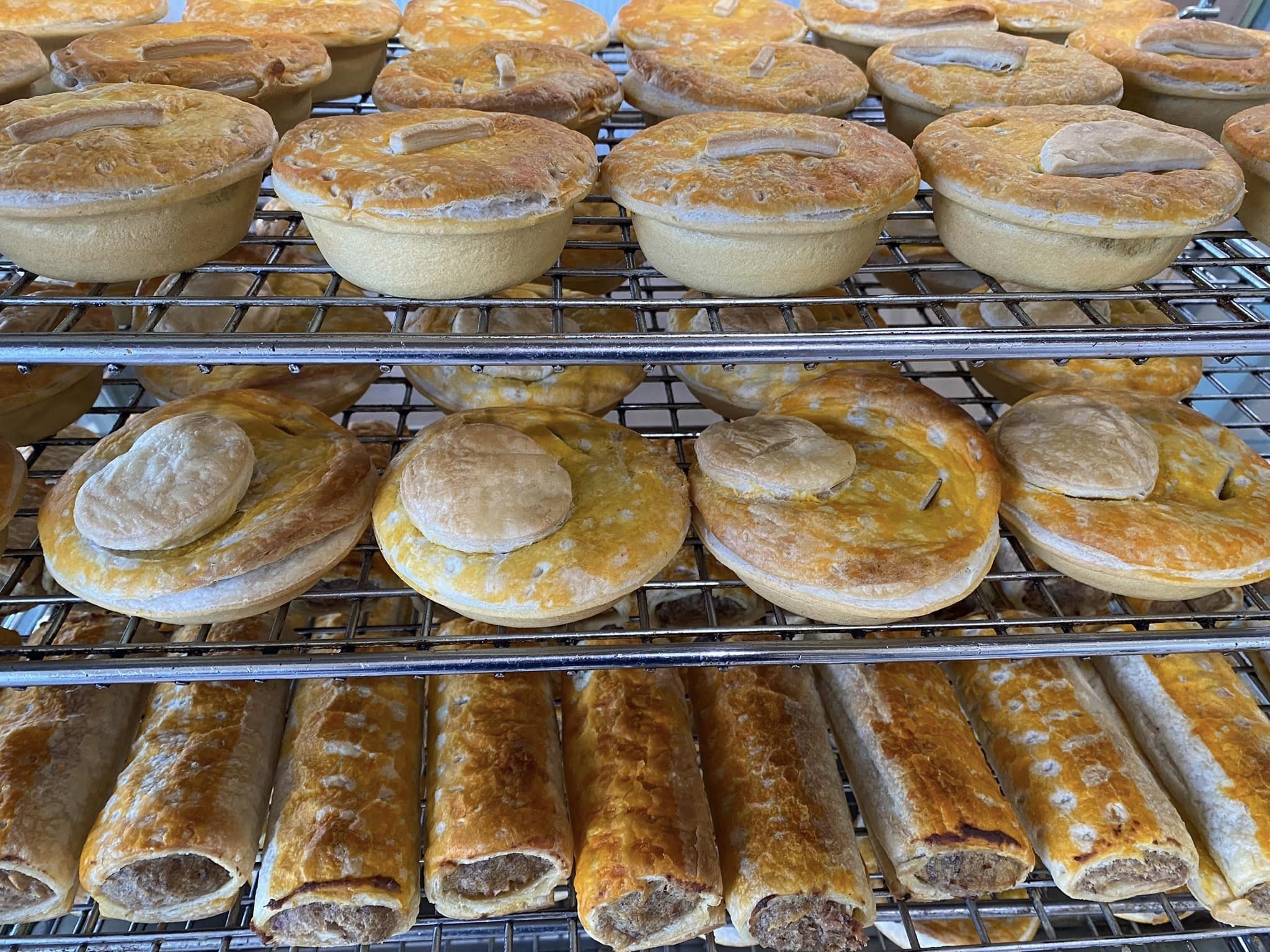 Various meat pies and sausage rolls placed on a metal cooling rack in a bakery