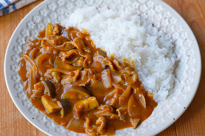 カレーライスが盛られたお皿がテーブルに置かれており、その横にはスプーンとガラスの水がある。