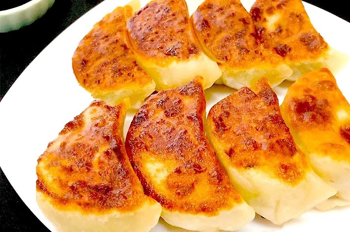 皿に盛られた焼き餃子が並んでいる。左上には小皿に入ったタレと箸が置かれている。