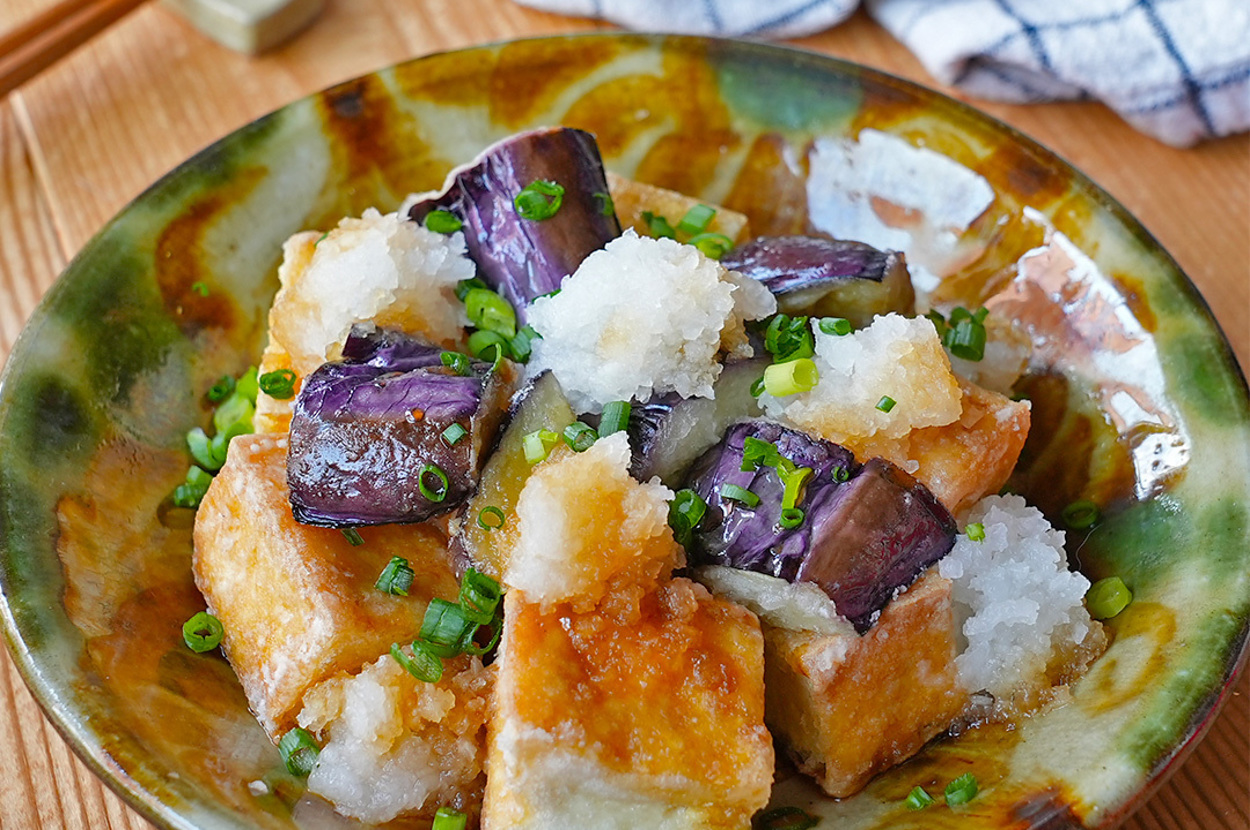 揚げ出し豆腐と茄子の和風料理が盛られた皿。背景に布巾と割り箸。