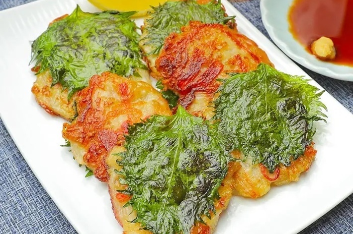 お皿に盛られた料理。鶏肉に大葉がのって調理されている。横にはレモンのくさびと小皿に入った醤油とワサビがある。