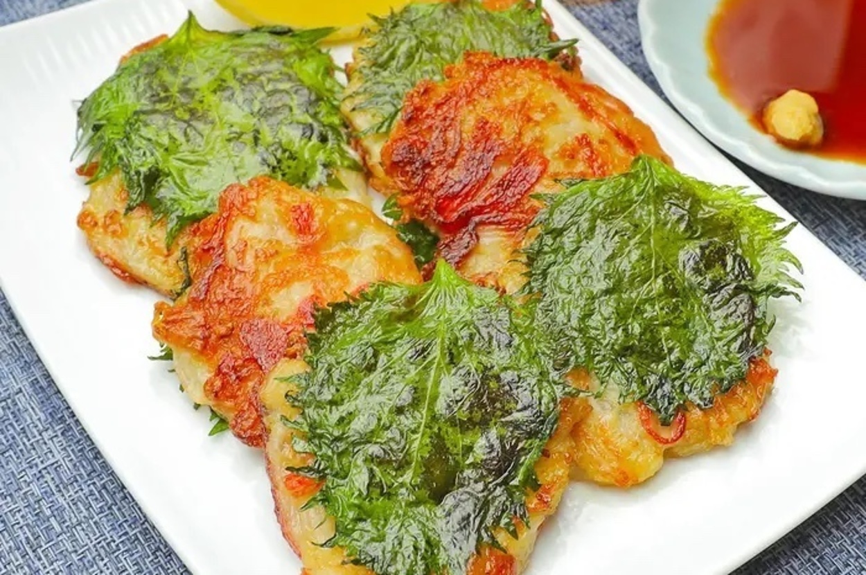 お皿に盛られた料理。鶏肉に大葉がのって調理されている。横にはレモンのくさびと小皿に入った醤油とワサビがある。