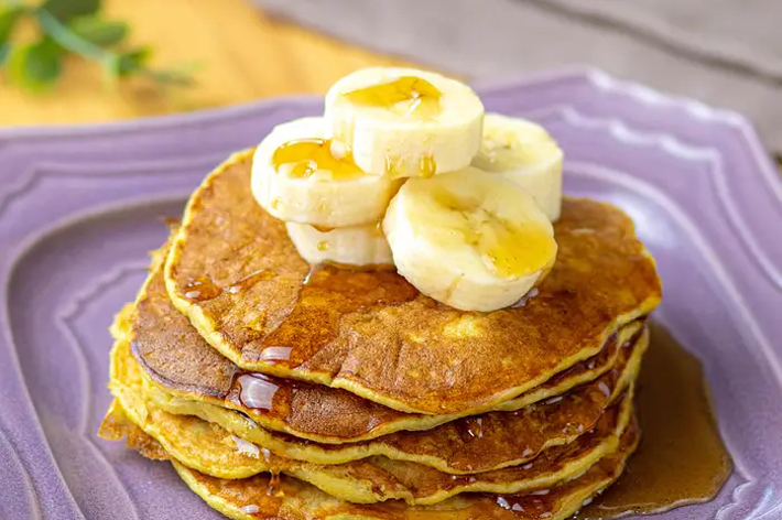 パンケーキ4枚が積み重なっており、上にスライスしたバナナとシロップがかかっている。