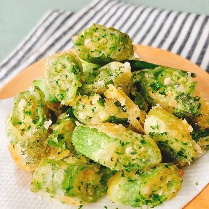 オクラの天ぷらが盛り付けられた皿。背景にはストライプの布が置かれている。