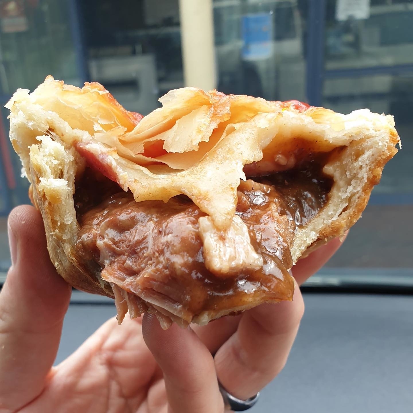Close-up of a hand holding a meat pie with a bite taken out, revealing its filling