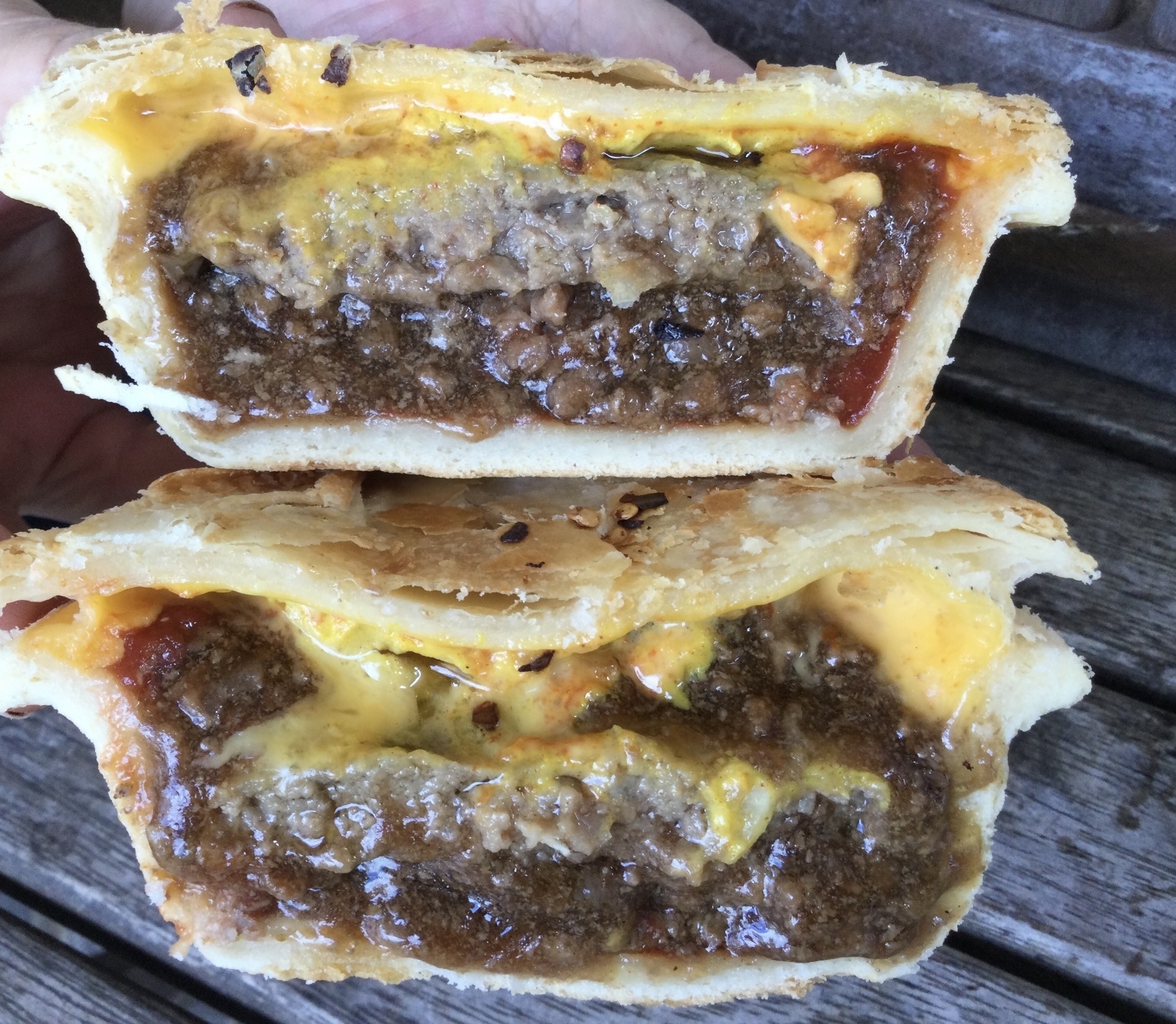 Cross-section of a savory pie showing layers of beef, cheese, and sauce, with a golden pastry crust