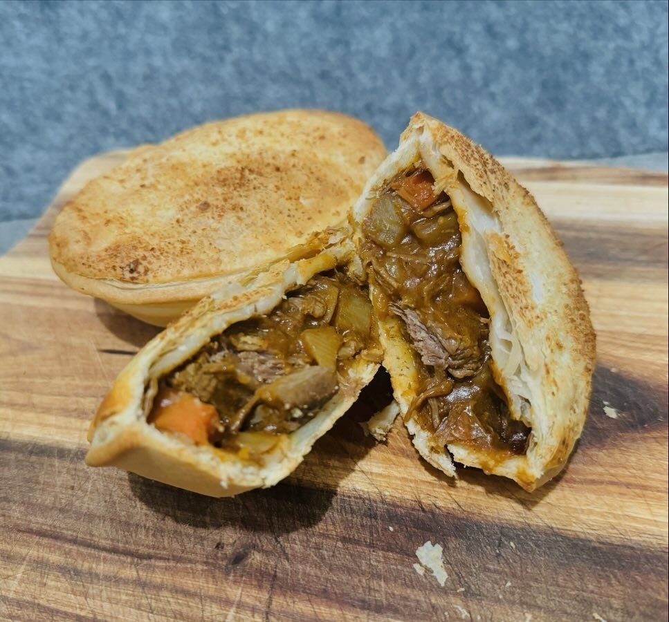 A savory meat pie is cut in half to reveal its filling of meat and vegetables on a wooden cutting board
