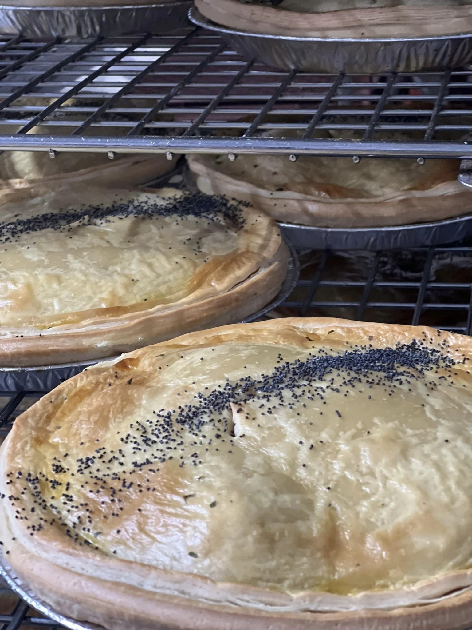Four freshly baked pies with golden-brown flaky crusts topped with poppy seeds inside a commercial oven