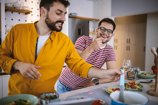 Two men cook in a modern kitchen, one eats
