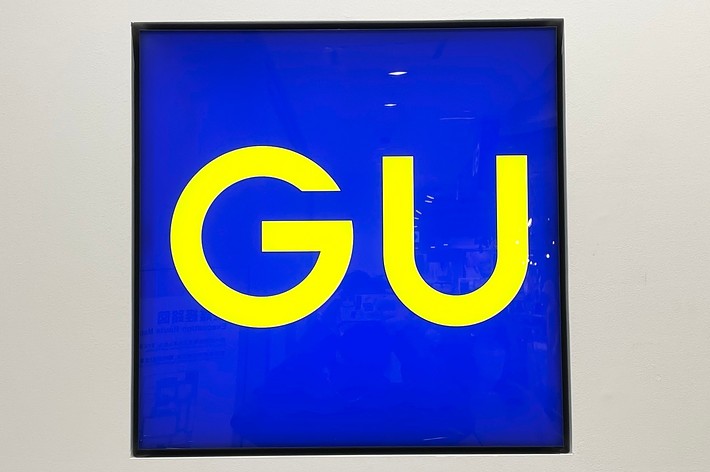 Square sign with large, yellow letters &ldquo;GU&rdquo; on a blue background inside a black frame